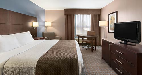 A spacious king accommodation at the Days Inn Stephenville featuring a comfortable bed, an arm chair & more